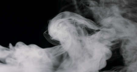 wispy smoke rolling along the bottom of the frame, against a black background.の写真素材