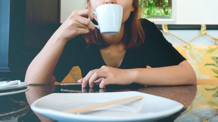 Closeup of a woman holding  coffee cup.at the table with dish Empty plate Get foodの写真素材