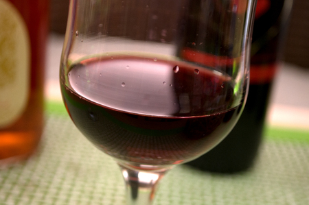 Half full glass of fresh delicious red wine, bottles in the background with heart, Novi Sad, Serbia