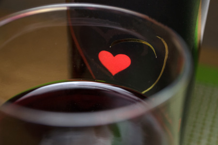Half full glass of fresh delicious red wine, bottles in the background with heart, Novi Sad, Serbiaの写真素材