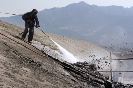 Worker on top of factory hall, with high pressure washer, cleans layer of old concreteの写真素材
