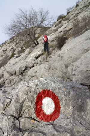 Climber with red backpack following the markings on the hard rocky terrain on the mountain Mosor in Croatiaの写真素材
