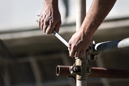 Worker with wrench in his hands builds iron scaffold on construction site の写真素材