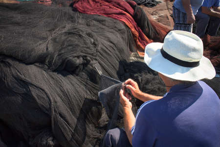 Needle with thread in fisherman hands repairing net for catching sardine