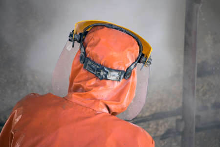 Worker in orange protective suit cleans corrosion damaged concrete bridge pillar with high pressure washerの写真素材