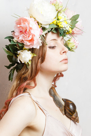 calm pretty girl with snail and flower crown on head on white backgroundの写真素材