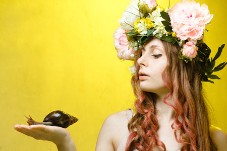 calm pretty girl with snail in hand and flower crown on head on yellow backgroundの写真素材
