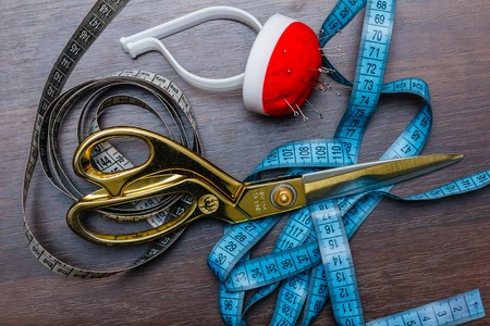 Professional tailor's tools for cutting and sewing, scissors, flexible ruler tape, niddles on the wooden tableの写真素材