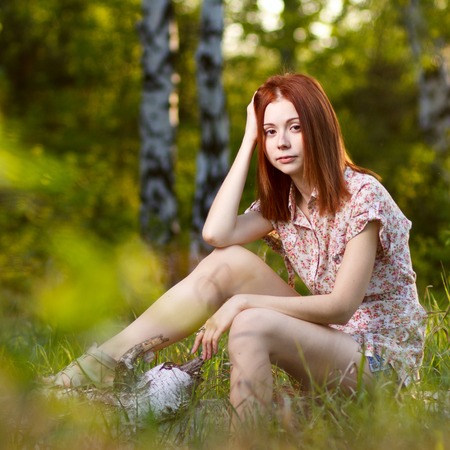 Beautiful redhead girl walking under the rays of the sunset in summer spring forestの写真素材