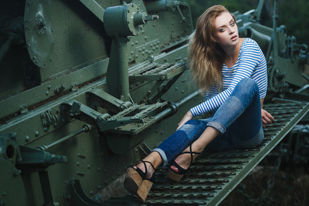 Young sexy woman model in jeans and striped tank top posing for fashion portrait near old artillery gun outsideの写真素材