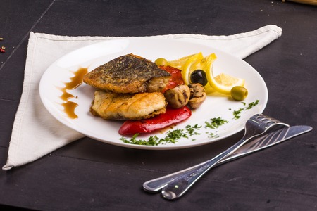 Concept: healthy food. Homemade grilled fish steak and vegetables on a plate with ingredients and cutlery aroundの写真素材