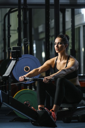 Concept: power, strength, healthy lifestyle, sport. Powerful attractive muscular woman CrossFit trainer do workout on indoor rower at the gymの写真素材