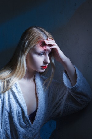 Concept: victim, accident, domestic violence. Beautiful young woman in bathrobe suffer head trauma in dramatic light.の写真素材