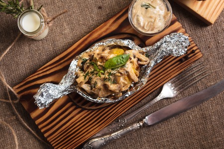 Concept: restaurant menus, healthy eating, homemade, gourmands, gluttony. Baked potatoes with mushroom sauce served in foil plate with ingredients and vintage cutlery on sackcloth background.の写真素材