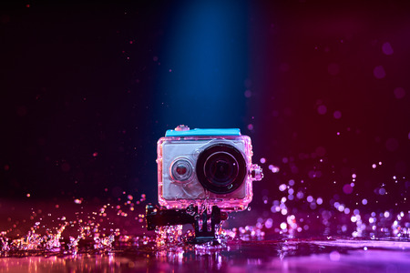 Concept: gear, gadget, action lifestyle, millennial. Vivid colorful shot of action camera in waterproof case splashed with water. Time freeze.の写真素材