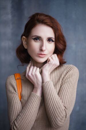 Concept: fashion, beauty. Pretty redhead thin lean young woman with vintage hairdo posing in knit dress. Studio photoshoot.の写真素材