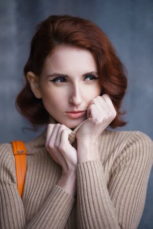 Concept: fashion, beauty. Pretty redhead thin lean young woman with vintage hairdo posing in knit dress. Studio photoshoot.の写真素材