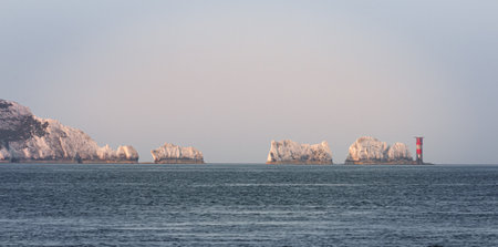 Sunrise projects warm glow on the Isle of Wight and Needles Lighthouse with calm sea and grey blue skyの写真素材