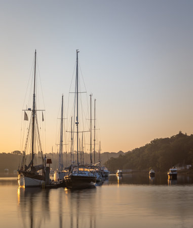 A sunrise scene of the Beaulieu River with sailing boats and pontoon. Misty haze in the background adds to the subtle, peaceful viewの写真素材