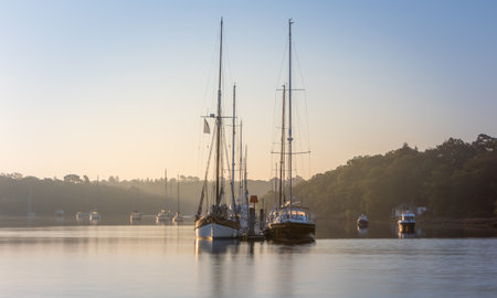 A sunrise scene of the Beaulieu River with sailing boats and pontoon. Misty haze in the background adds to the subtle, peaceful viewの写真素材
