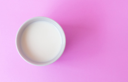 Closeup top view milk in white ceramic cup on pink background, selective focusの写真素材