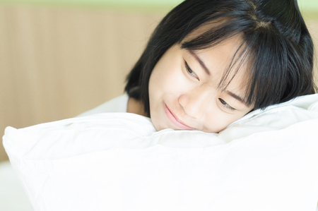 Closeup young woman hugging pillow with smile face and happy feeling lying on bedの写真素材