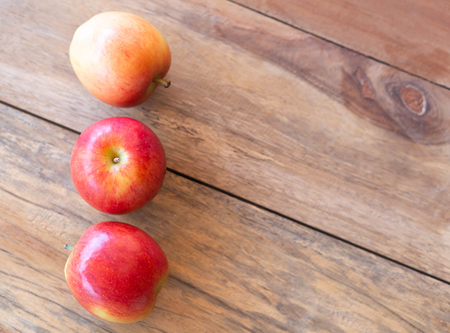 Closeup top view fresh red apples fruit on wood table background with light from out door, food healthy diet conceptの写真素材