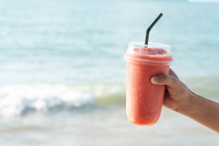Hand holding glass of strawberry smoothie with sea water background, Holiday and relax timeの写真素材