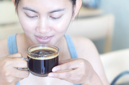 Closeup woman hand holding glass of hot americano coffee for drink with happy face feeling, selective focus, vintage toneの写真素材