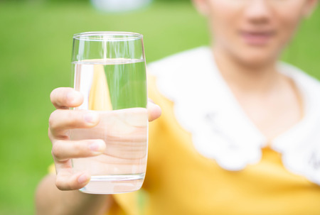 Hand holding glass of pure water on green nature background, healthy concept