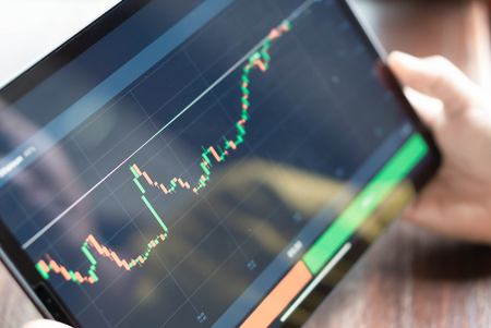 Closeup hand holding digital tablet computer with graph of Binary option for trading platform,...