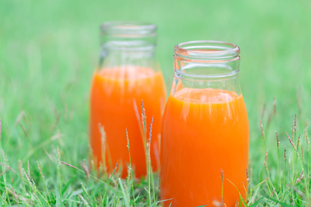 Closeup glass bottle of orange juice fruit on green grass nature background, food healthy conceptの写真素材