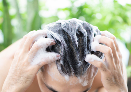 Closeup young man washing hair with shampoo outdoor, health care concept, selective focusの写真素材