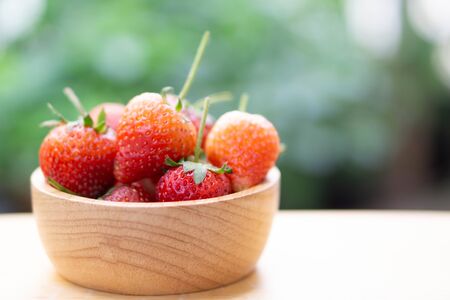 Closeup red strawberry in wood bowl with green nature background, selective focusの写真素材