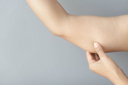 Closeup woman hand checking upper arm on grey background health care and medical conceptの写真素材