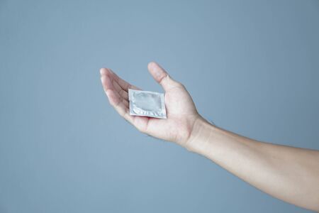 Close up man hand holding condom lying on white bed, health care and medical concept, selective focusの写真素材