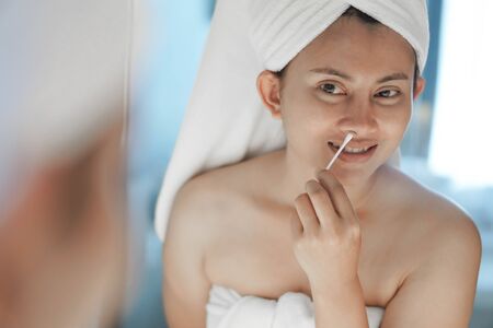 Close up woman looking her face in the mirror with cotton brush cleaning nose after bath, health care and beautyの写真素材
