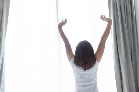 Close up woman sitting on the bed and stretching after waking up for relax in the morning with over light backgroundの写真素材