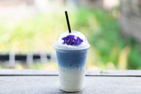 Closeup glass of ice butterfly pea latte on wood table with nature backgroundの写真素材