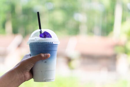 Closeup hand holding glass of ice butterfly pea latte with nature backgroundの写真素材