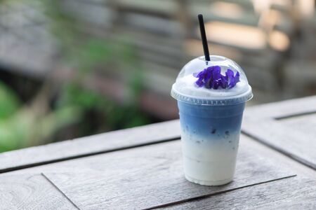Closeup glass of ice butterfly pea latte on wood table with nature backgroundの写真素材