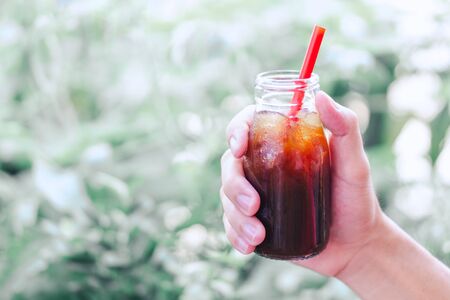 Close up hand holding bottle glass of americano coffee with green nature background, vintage toneの写真素材