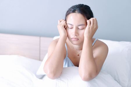 Closeup woman sitting on bed in the bedroom with thinking or depressed feeling, selective focusの写真素材