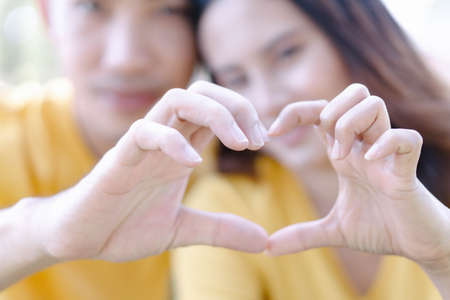Closeup of couple making heart shape with hands in the parkの写真素材