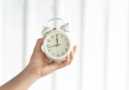 Closeup hand holding alarm clock on white background, Time to wake upの写真素材