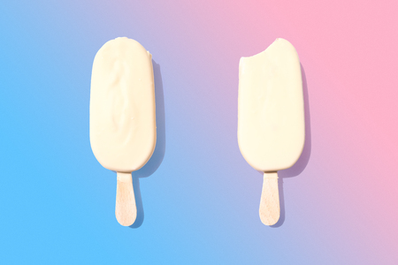 Two white chocolate icecreams on stick placed on pink and blue gradient backgroundの写真素材
