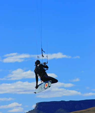 A kiter jumping and doing a grab with mountain range below and blue sky and clouds as backgroundの写真素材