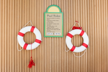 Swimming pool rules hang on the wall with lifebuoys