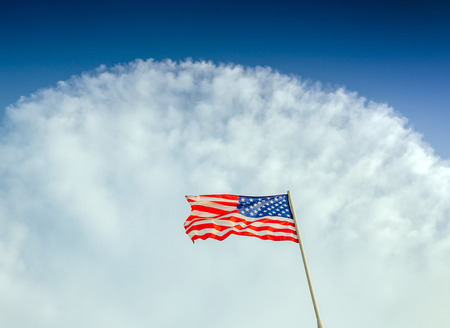 American flag flapping against cloudy blue sky, focus on star of waving flagの写真素材