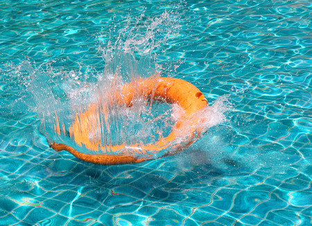 Orange life buoy splash water in the clear blue swimming pool, for the emergence caseの写真素材